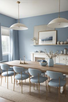 a dining room table with blue chairs and white lamps hanging from it's ceiling