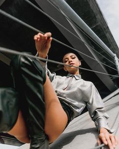 a woman sitting on top of a roof next to a tall building and holding her hand up