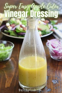 a bottle filled with dressing sitting on top of a wooden table next to plates of salad