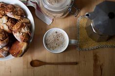 there is a bowl of cinnamon rolls next to a cup of coffee and a teapot