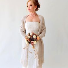 a woman in a white dress holding a flower bouquet and wearing a cardigan over her shoulders