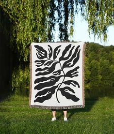 a woman standing in the grass holding up a black and white blanket with leaves on it