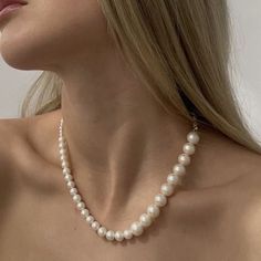 a woman wearing a white necklace with pearls on the bottom of her neck and shoulder