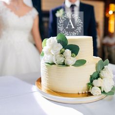 a bride and groom standing behind a white wedding cake with greenery on the top