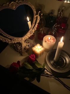 candles and roses on a table in front of a heart - shaped mirror with a lit candle