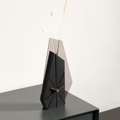 a black clock sitting on top of a table next to a plant in a vase