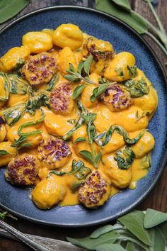 a blue plate topped with yellow food covered in sauce and vegetables next to green leaves