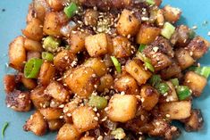 a blue plate topped with fried tofu and green onions covered in sesame seed flakes