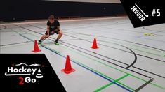 a man in black shirt and orange cones on an indoor hockey rink with neon lines