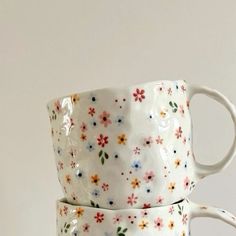 two coffee mugs are stacked on top of each other with colorful flowers painted on them