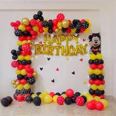 a mickey mouse balloon arch with the words happy birthday written in gold, black and red