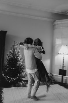 black and white photograph of two people hugging in front of a christmas tree