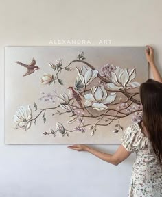 a woman is standing in front of a wall painting with flowers and birds on it