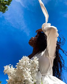 a woman in white dress holding flowers up to the sky with her arms stretched out