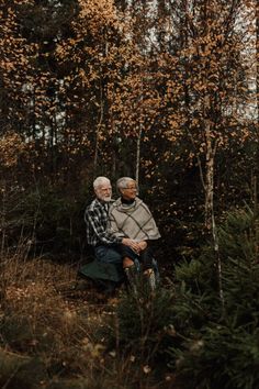 an older couple sitting on a bench in the woods