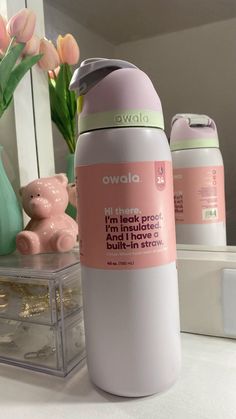 a pink and white bottle sitting on top of a counter next to a vase with flowers