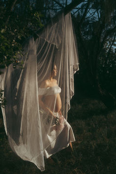 a woman in white dress standing under a sheer curtain