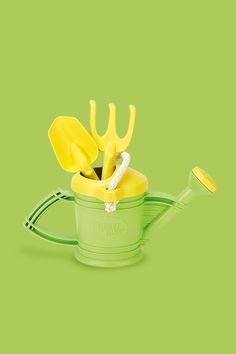 a green watering can with yellow gardening utensils in it's top handle