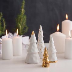 small white christmas trees with gold accents and candles in front of them on a table