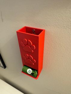 a red box with a paw print on it is attached to the wall by a magnet