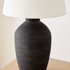 a black vase sitting on top of a wooden table next to a white lampshade