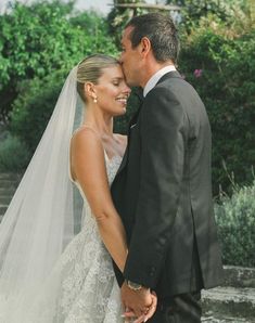 a bride and groom standing next to each other in front of some steps with trees