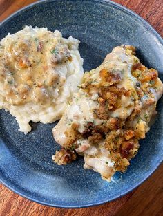 a blue plate topped with mashed potatoes and meat covered in gravy on top of a wooden table