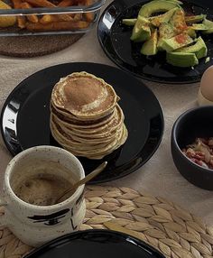 pancakes, avocado and other food are on black plates next to each other