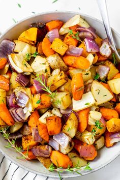 a white bowl filled with potatoes and carrots next to a fork on a table