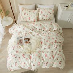 a white bed with pink flowers on it and a magazine laying on the comforter