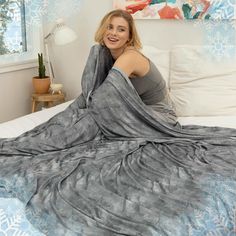 a woman laying on top of a bed covered in a gray blanket and smiling at the camera