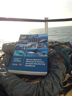 a book sitting on top of a boat next to the ocean in front of a rope