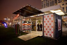 an outdoor booth at night with people standing around it and lights on the building in the background