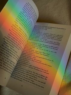 an open book sitting on top of a bed next to a rainbow colored wallpaper