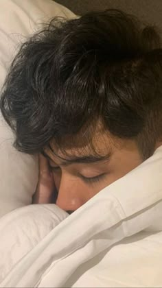 a young man sleeping in bed with his head on the pillow