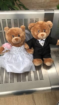 two teddy bears dressed in wedding attire sitting on a metal bench next to each other