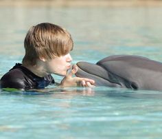 a young boy is playing with a dolphin in the water while it's swimming