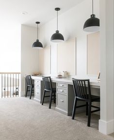 two black chairs are sitting in front of a desk with three lights hanging above it