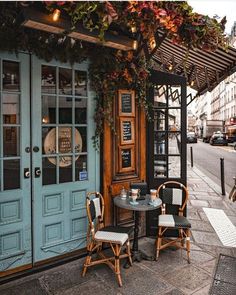 two chairs sitting at a table in front of a building with blue doors and windows