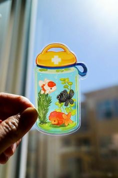 a hand holding up a sticker with fish and plants on it