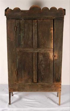 an old wooden cabinet with four doors and two legs, on a white sheeted surface