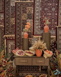 an assortment of fruits and vegetables on display in front of a wall covered with rugs