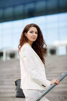 a woman with long hair in a white suit and black purse is standing on steps