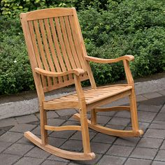 a wooden rocking chair sitting on top of a brick walkway next to bushes and shrubbery