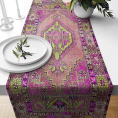 a pink table runner with green and purple designs on it next to a white plate