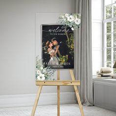 an easel with a wedding photo and flowers on it in front of a window