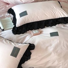 three pillows with black ruffles and white sheets on top of each other in front of a book