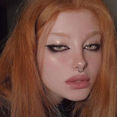 a woman with long red hair and piercings on her nose is looking at the camera