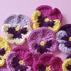 several crocheted flowers are arranged on a pink surface with yellow, purple and white petals