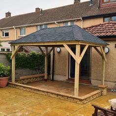 a wooden gazebo sitting on top of a patio next to a brick wall and potted plants